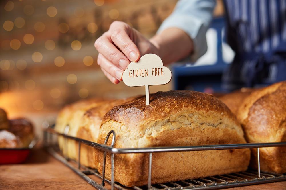 Sales assistant in bakery putting gluten free label into freshly baked baked sourdough loaves of bread