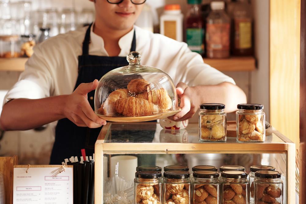 Cafe waiter putting plate with fresh croissants on counter to sell