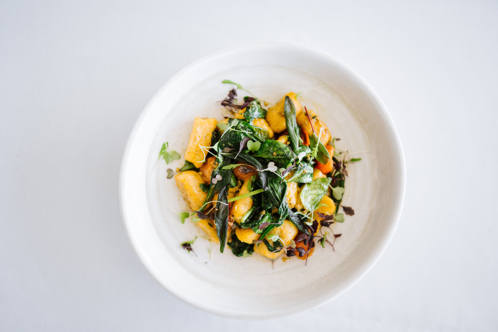 A top view of a gourmet dish with gnocchi and fresh greens on a white plate, set against a white background
