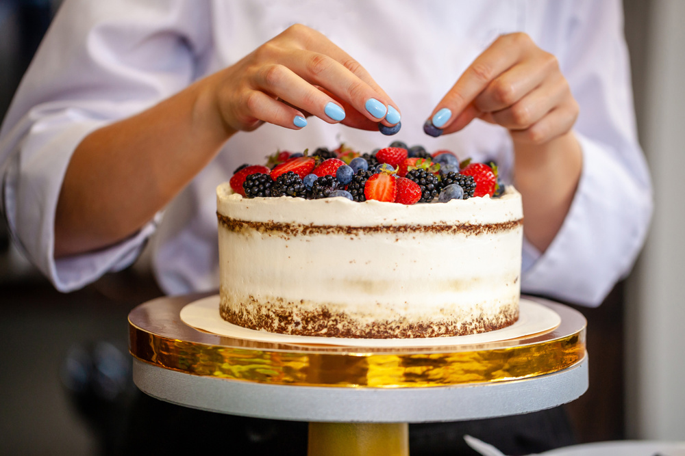 A baker decorating a cake by putting berries on top